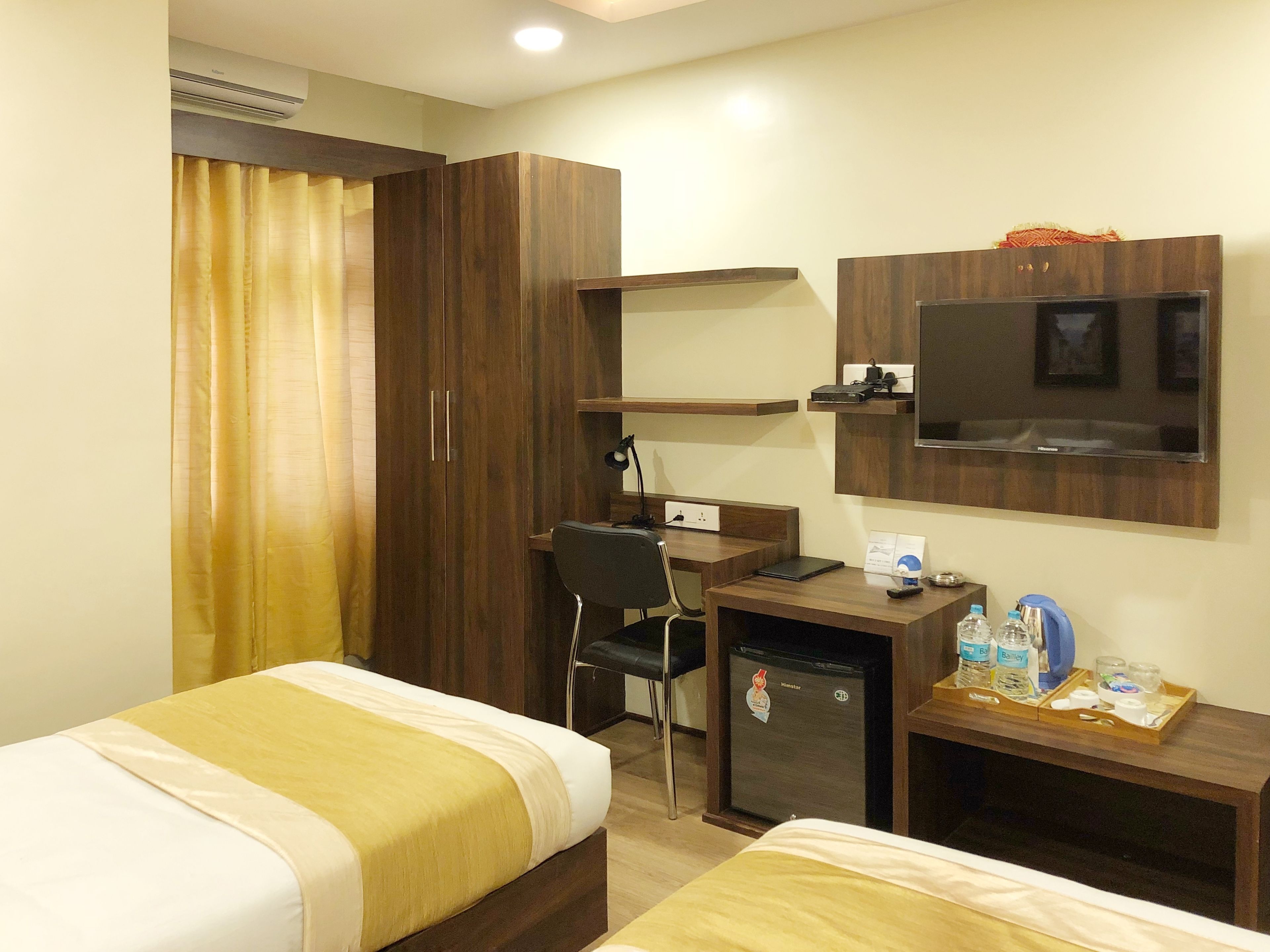 Habitación de hotel con dos camas individuales, un escritorio con silla, televisor, minibar y armario.