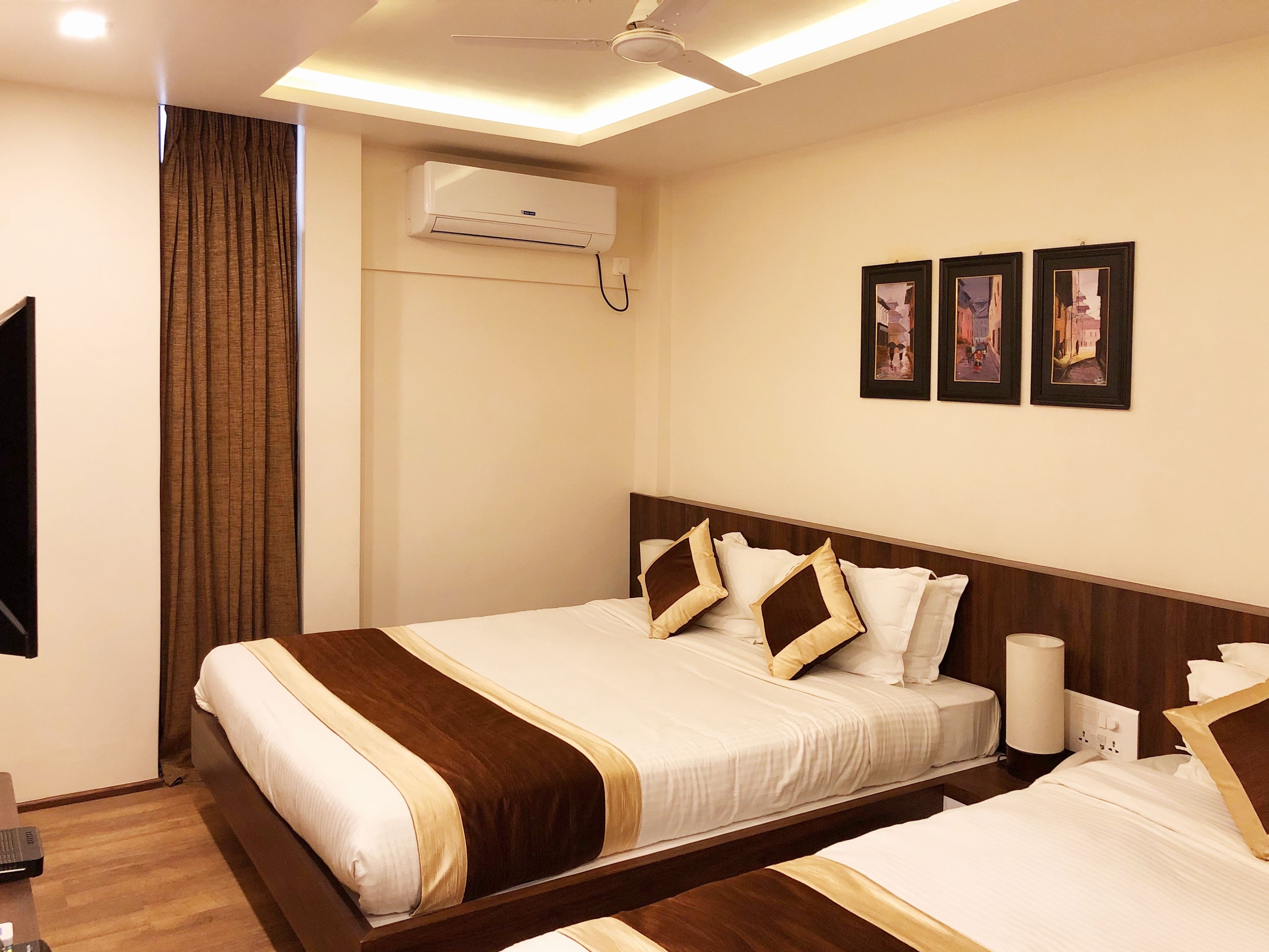 Ein Hotelzimmer mit zwei Betten, einem Deckenventilator, einer Klimaanlage und gerahmten Bildern an der Wand.
