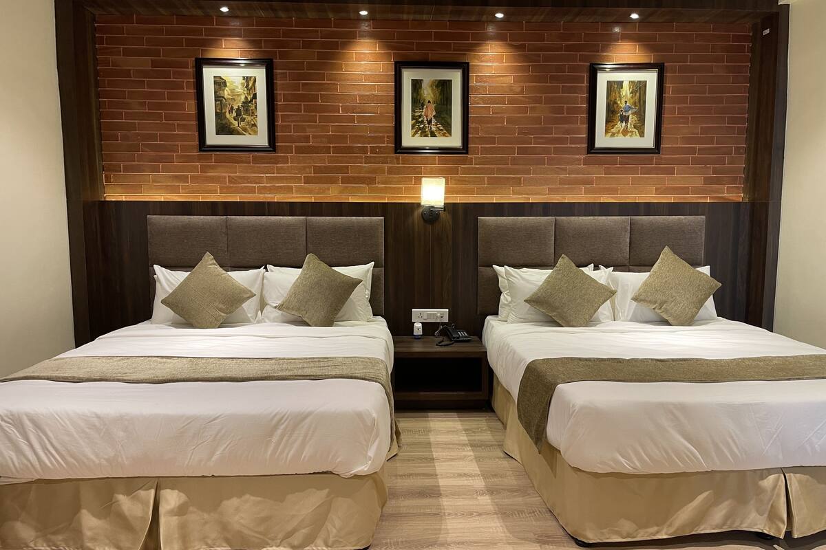 A hotel room with two beds, a brick wall, and framed artwork above the beds.