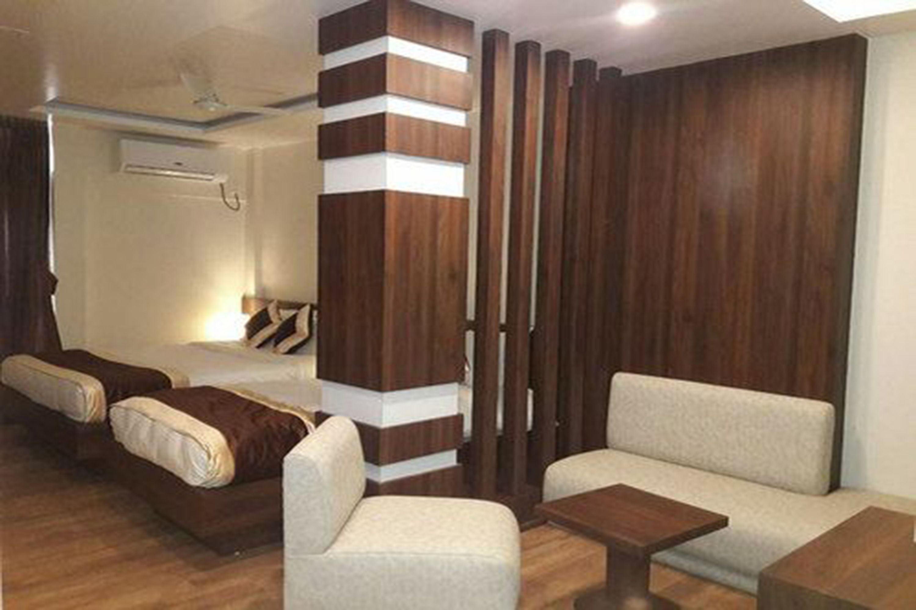 A hotel room with a bed, two sofas, a small table, and a wooden partition.