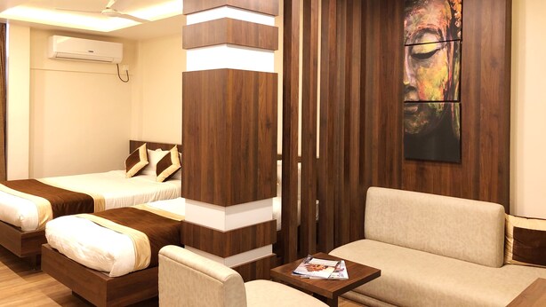 A hotel room with two beds, a sofa, a coffee table, and a large abstract painting on the wall. - Hotel Kailash (Birgunj)