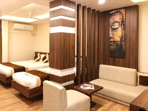 A hotel room with two beds, a sofa, a coffee table, and a large abstract painting on the wall. - Hotel Kailash (Birgunj)