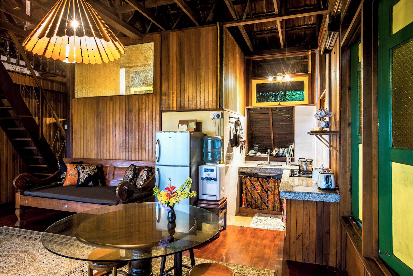 A cozy cabin interior with a wooden interior, a dining table with a vase of flowers, a kitchen area with a water dispenser, and a staircase.