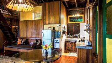 A cozy cabin interior with a wooden interior, a dining table with a vase of flowers, a kitchen area with a water dispenser, and a staircase.