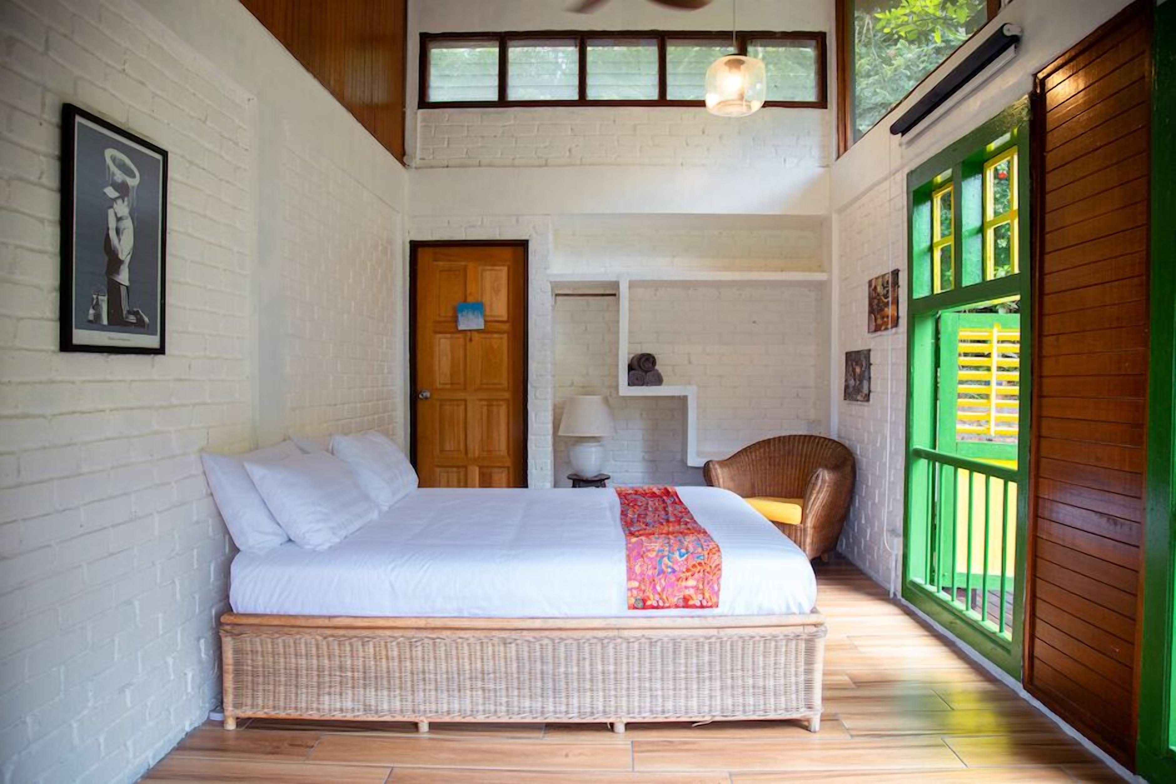 A bedroom with a bed, a chair, a lamp, and a window with green shutters.