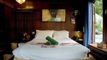 A wooden-paneled room with a bed, a framed artwork, a nightstand, a lamp, and a window with a view of greenery.