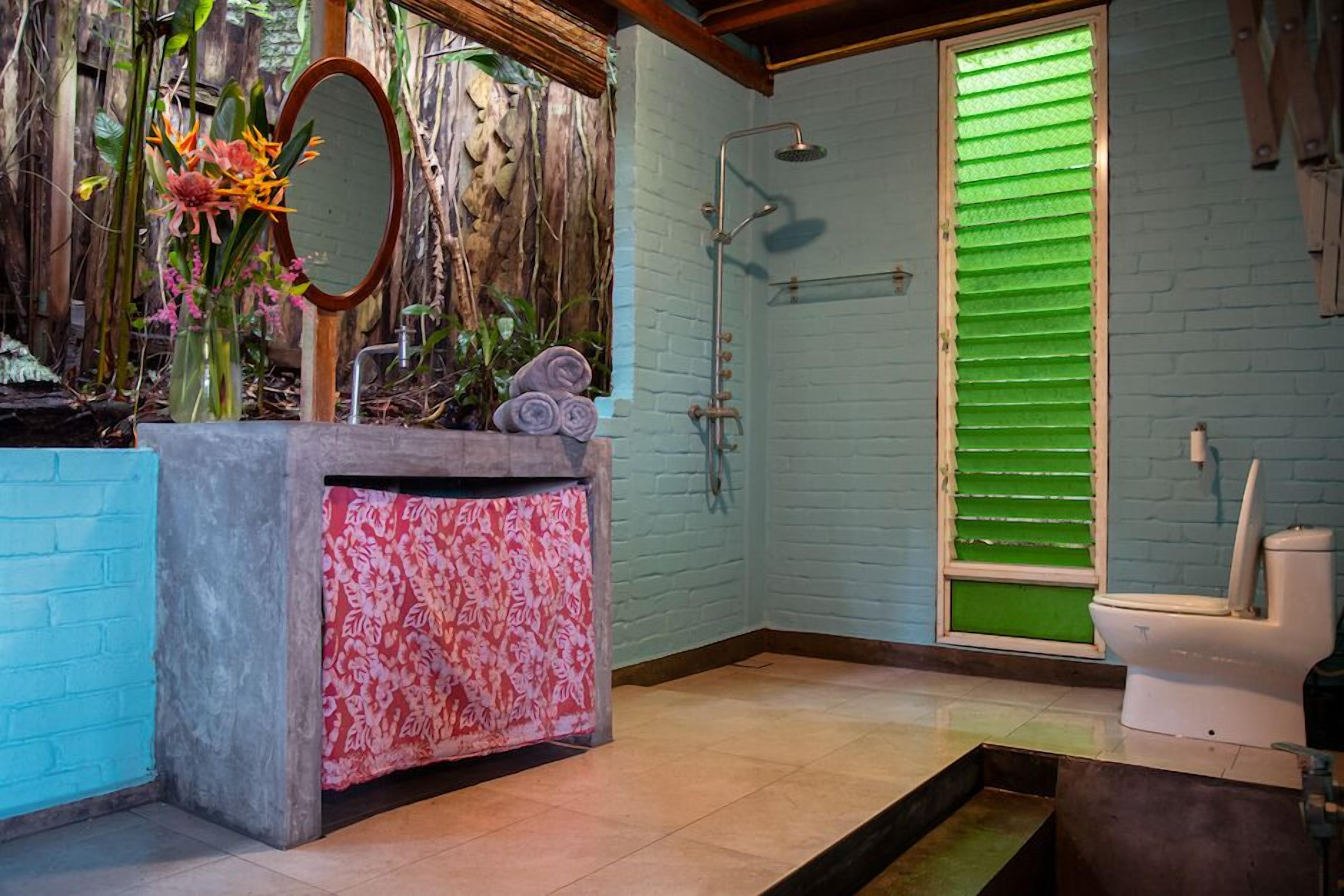 A bathroom with a shower, toilet, and a sink area with a mirror and decorative plants.