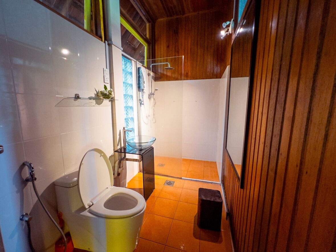 Et kompakt badeværelse med toilet, glasbrusekabine og trævæg.
