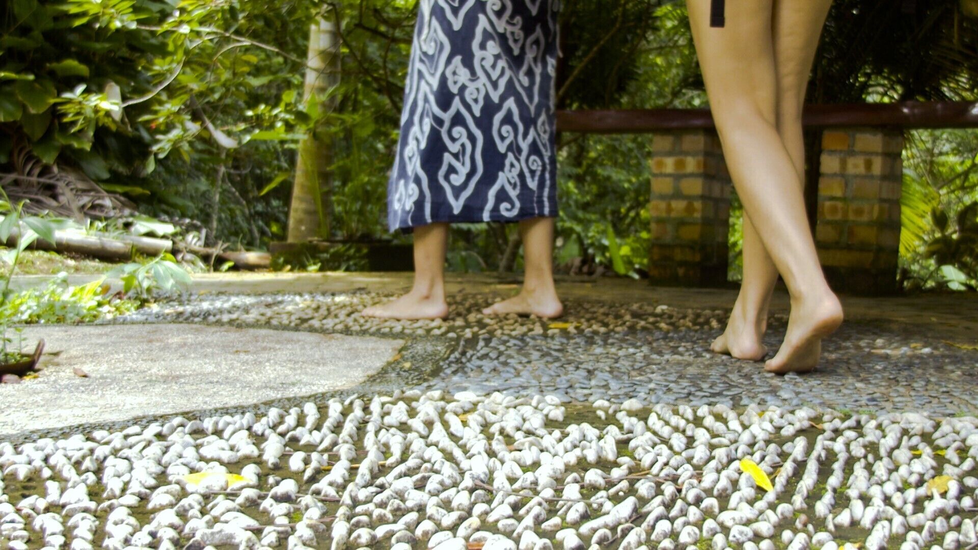 A tiled pathway with pebbles and a patterned fabric draped over a railing.