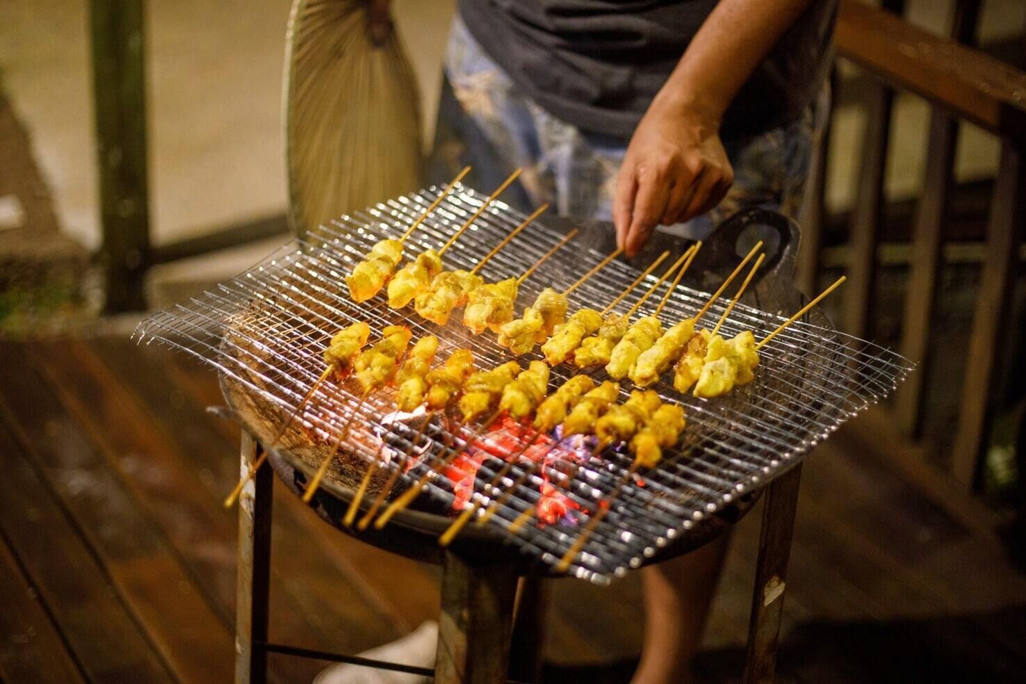 A person grilling skewers on an outdoor grill.