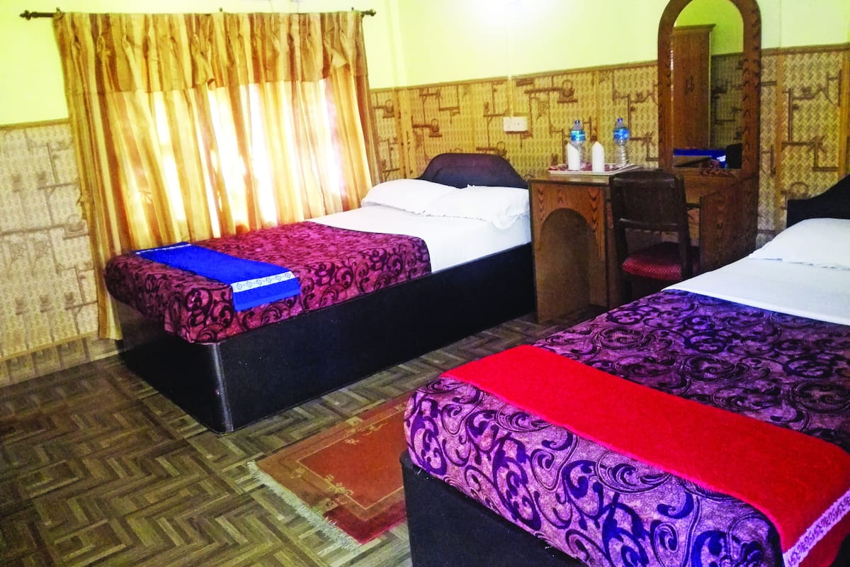 Two single beds with patterned bedspreads, a wooden desk with a chair, a mirror, and a wall-mounted air conditioner.