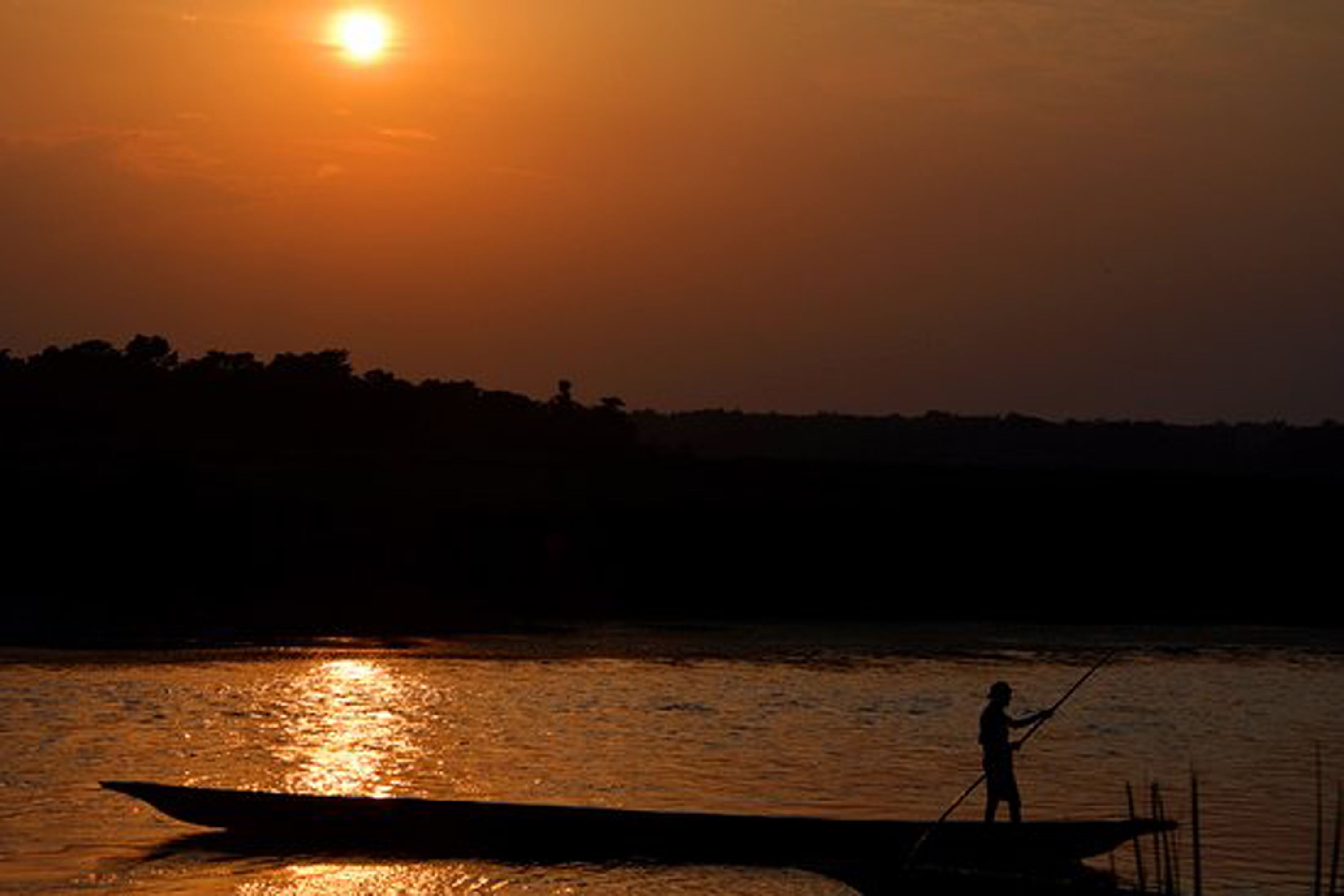 A silhouette of a person fishing on a boat at sunset.