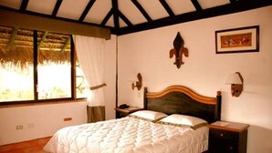 A bedroom with a bed, a nightstand, a wall-mounted lamp, and a window with curtains. - Rainbow Safari Resort (Sauraha)