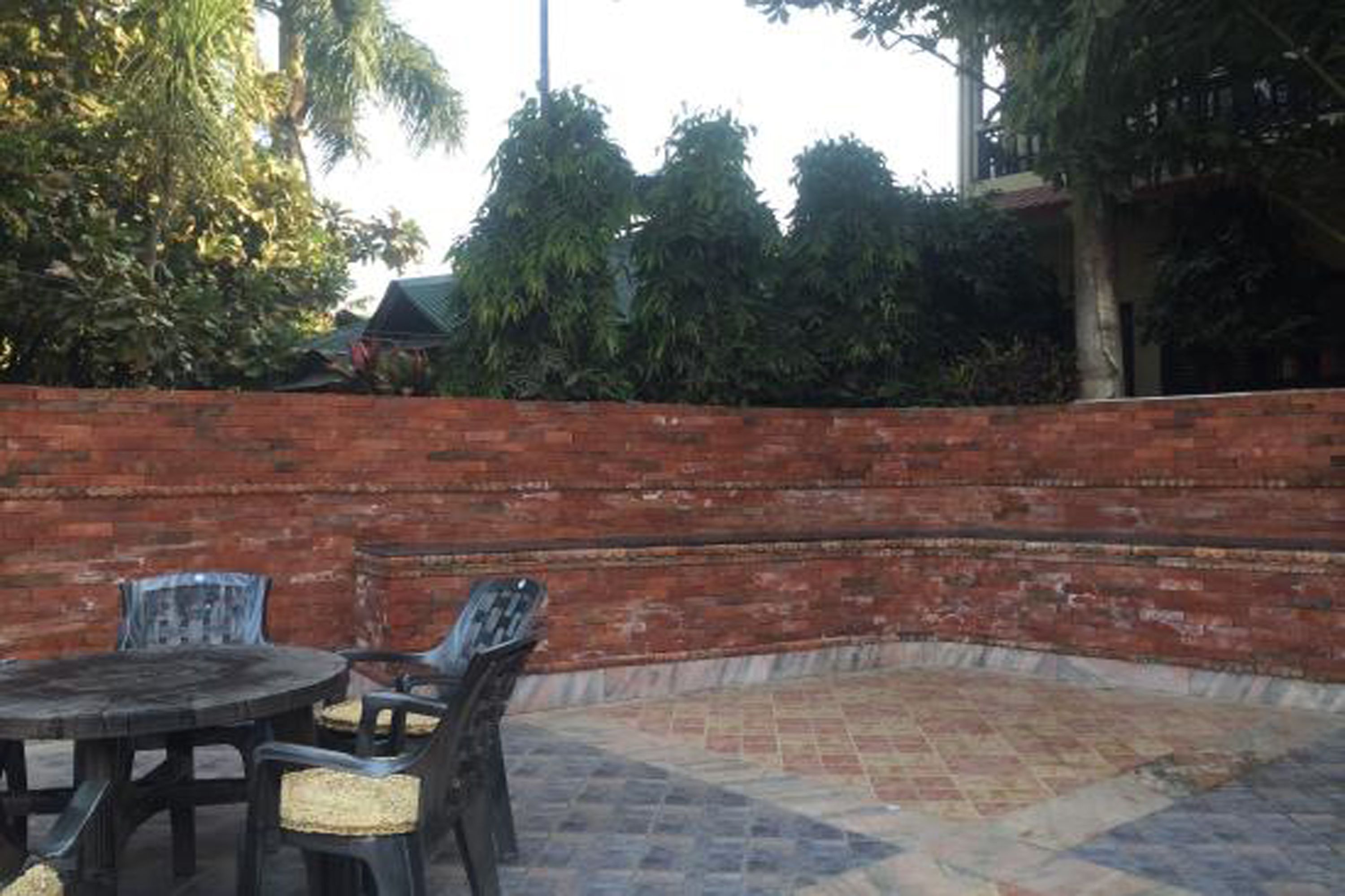 An outdoor patio with a brick wall, a round table, and chairs.
