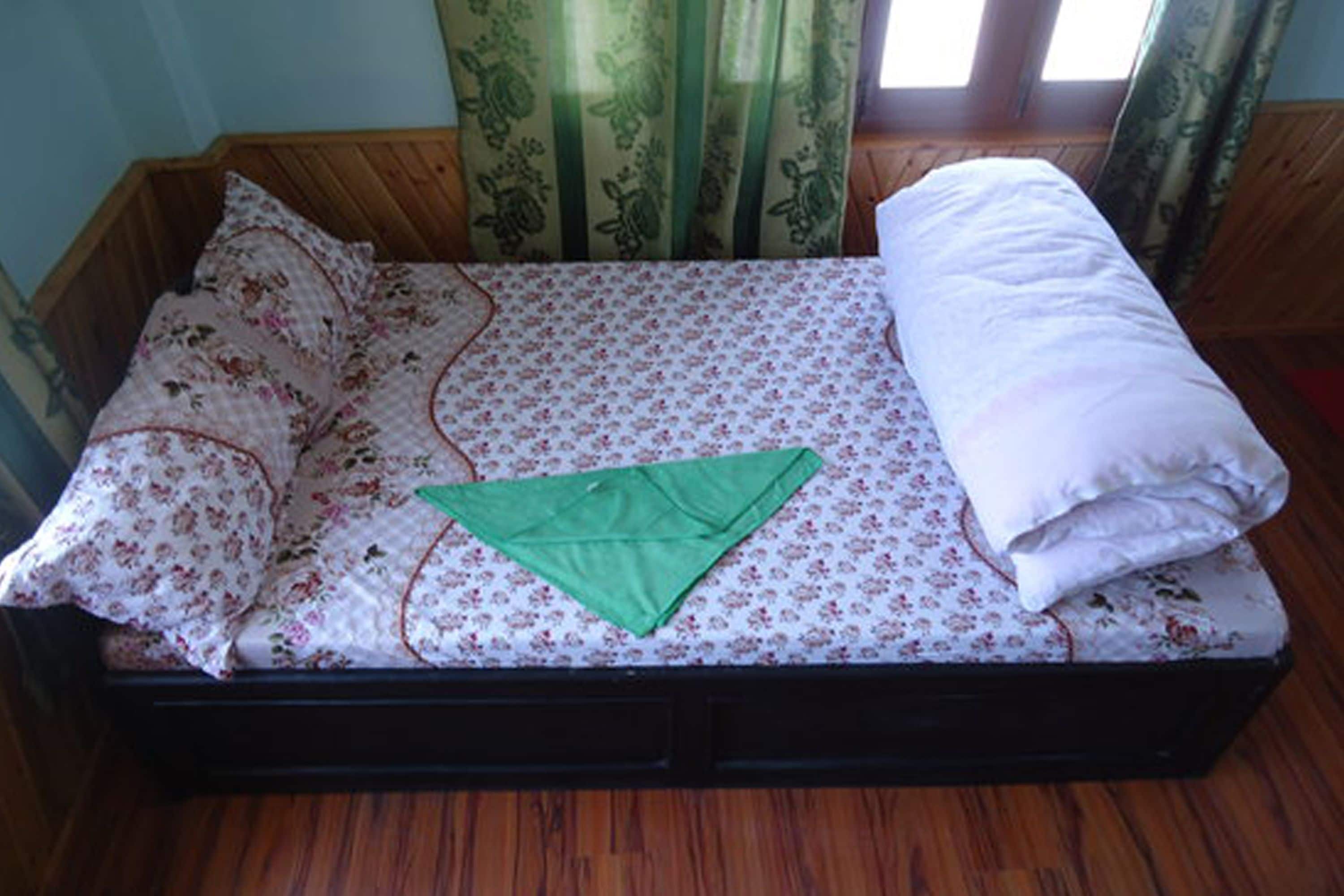 Una cama individual con una colcha estampada y un objeto verde doblado encima, además de una almohada blanca.