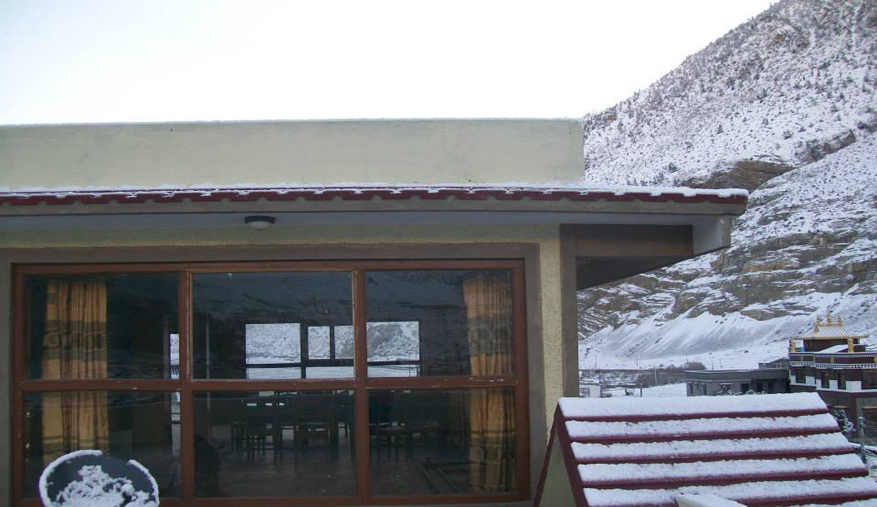 Un edificio con amplias puertas y ventanas de vidrio, un balcón cubierto de nieve y un paisaje montañoso al fondo.