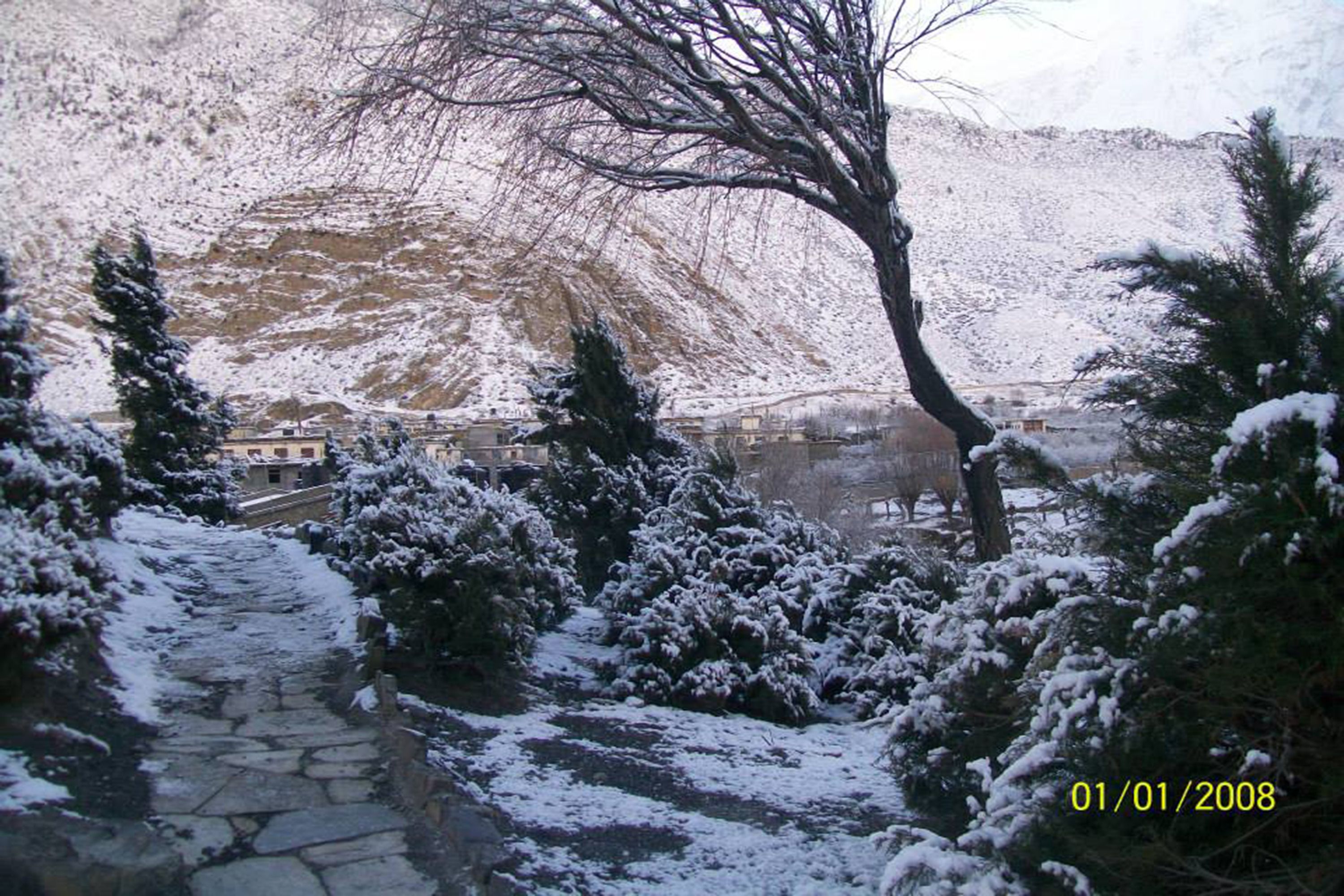 A snow-covered stone pathway leading to a building with a mountainous backdrop.