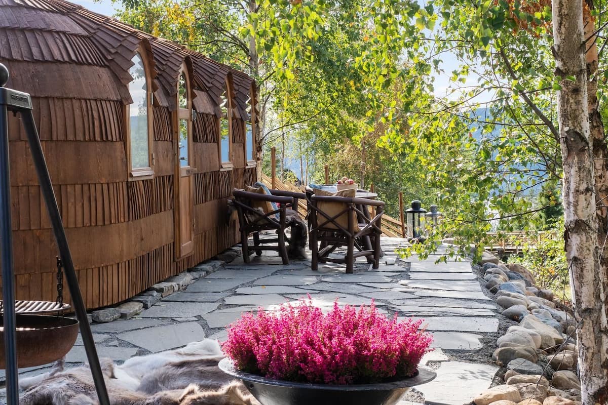 A rustic wooden building with a thatched roof, a stone pathway, and a table with chairs.