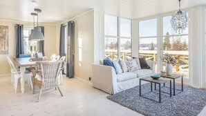 A bright, spacious living area with a dining table, wicker chairs, a sofa, and a view of a wooden deck through large windows. - Villa Heidi (Stange)
