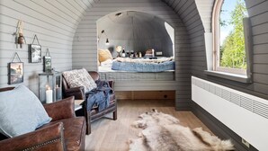 A loft bedroom with a curved ceiling, a bed with a fur throw, a leather chair, a fur rug, and a window with a view of greenery. - Villa Heidi (Stange)