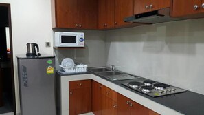 A compact kitchen with a refrigerator, microwave, stove, and wooden cabinets. - The Supara (Bangkok)