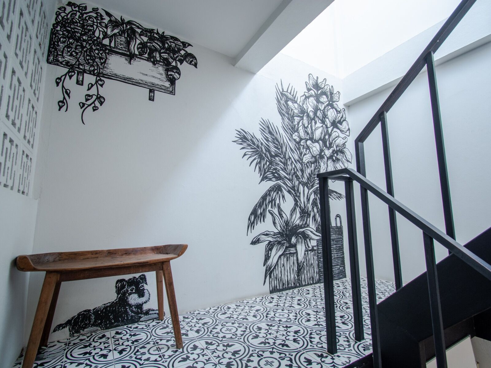 Una escalera con barandilla negra, un banco de madera y un muro con baldosas de diseño blanco y negro.