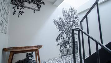 Una escalera con barandilla negra, un banco de madera y un muro con baldosas de diseño blanco y negro.
