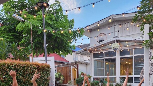 An outdoor yoga class in a courtyard with string lights, a building with large windows, and a hedge. - Hostel Lullaby - Adults Only (Chiang Mai)