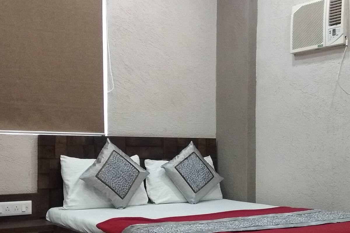 A bedroom with a bed, nightstands, a wall-mounted air conditioner, and a ceiling light fixture.