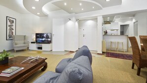 Una sala de estar moderna con un sofá, una mesa de centro, un televisor y una cocina al fondo.