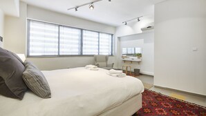 Una habitación de hotel moderna con una cama grande, un escritorio, una silla y una ventana con persianas.