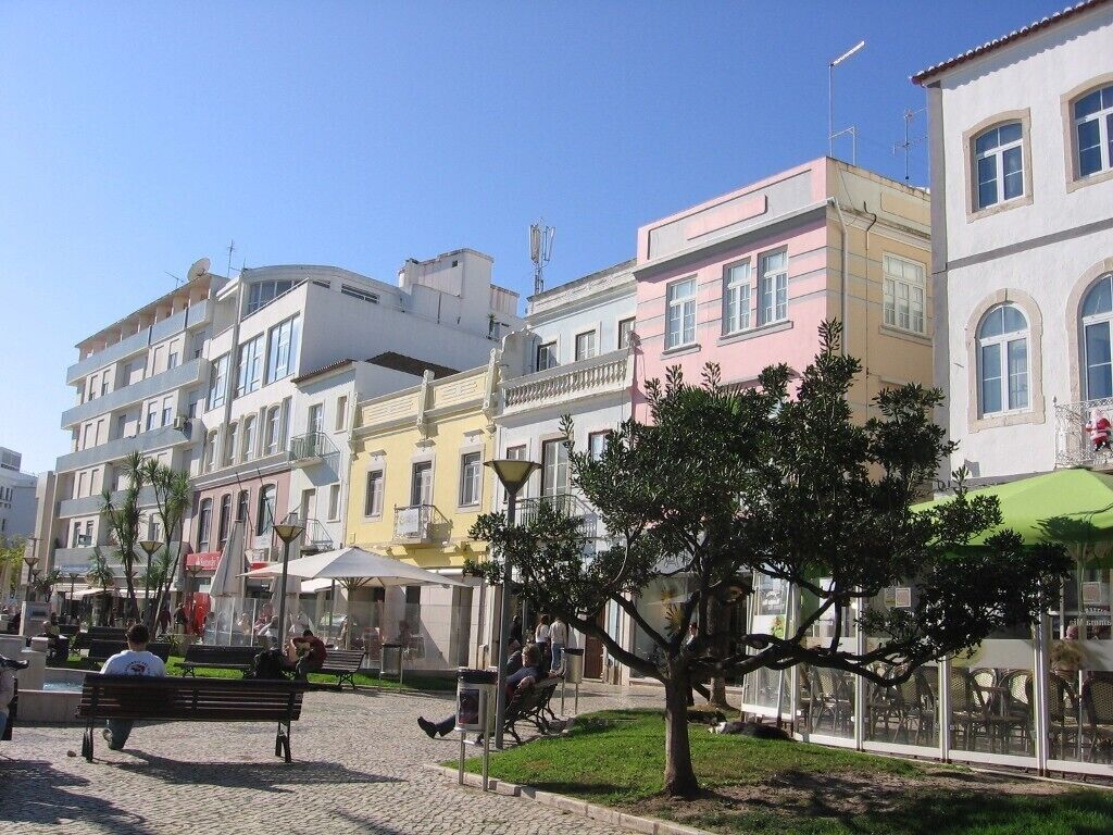 A street with colorful buildings, a bench, and a tree.