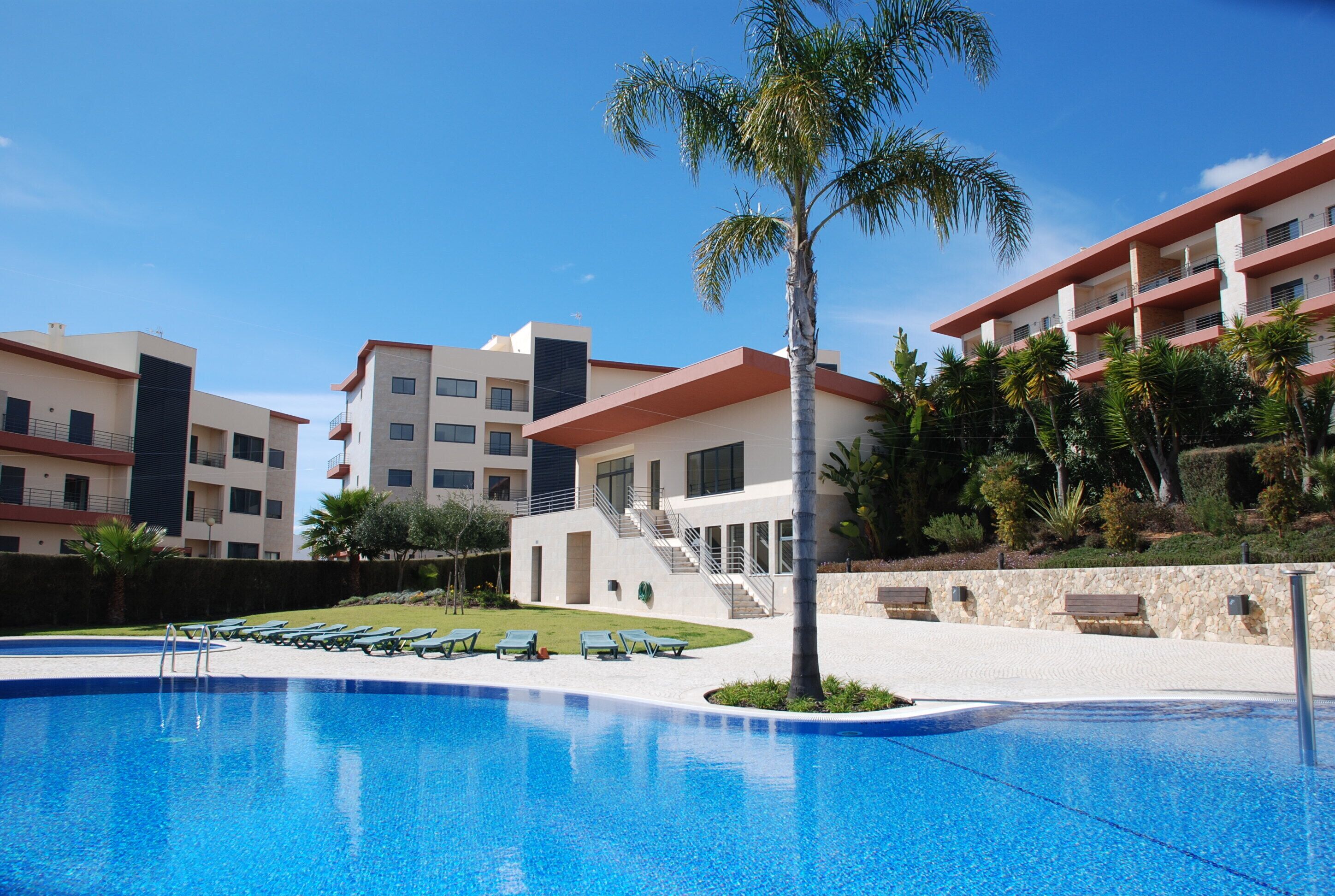 A modern hotel with a swimming pool, multiple balconies, and a well-maintained garden.