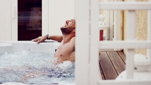 Una persona en un jacuzzi con una terraza de madera y barandilla blanca.