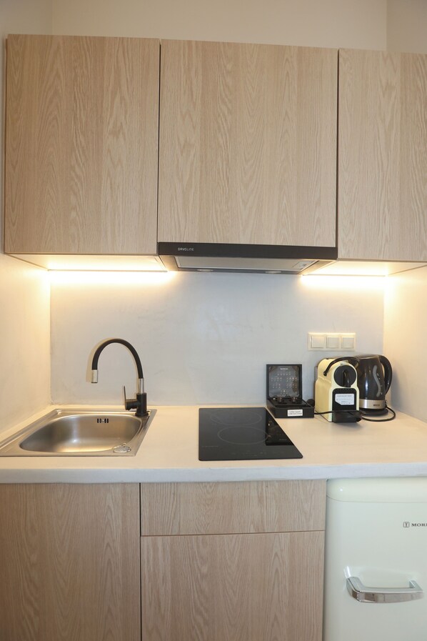 A modern kitchen with wooden cabinets, a stainless steel sink, a black induction cooktop, a coffee maker, and a white refrigerator. - Ventoura Studios & Apartments (Syros)
