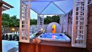 Un jacuzzi bajo una pérgola de madera con un muro de piedra de fondo.