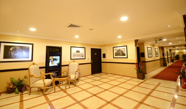 A hotel lobby with a checkered floor, framed pictures on the walls, a reception desk, and a seating area with chairs. - Qasr Al Sahab (Khamis Mushait)