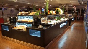 A buffet counter with various food items and a sign for Qasr Al'Abbar Hotel. - Qasr Al Sahab (Khamis Mushait)