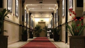 A hotel hallway with a red carpet, potted plants, and framed pictures on the walls. - Qasr Al Sahab (Khamis Mushait)