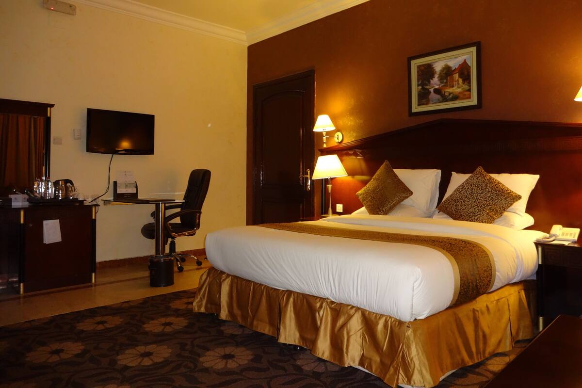 A hotel room with a large bed, a desk with a chair, a television, and a painting on the wall.