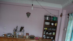 Une cuisine avec une table en bois, un saladier rempli de fruits et une bouteille posée sur la table. On y trouve également un meuble contenant des ustensiles et des récipients de cuisine.