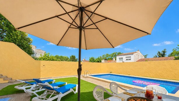 A poolside dining area with a table set for two, a pool, and lounge chairs. - Very spacious house with private pool, Barbecue and Wifi (l'Escala)