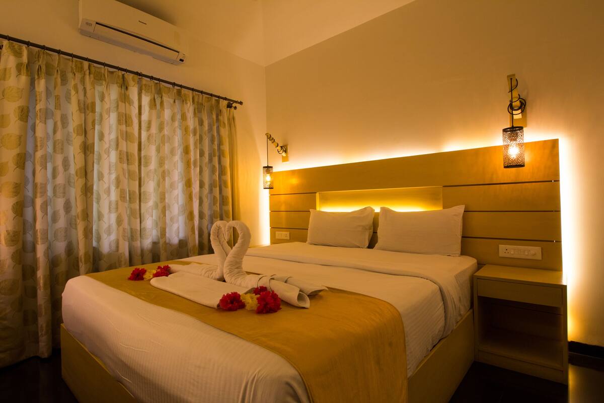 A hotel room with a bed, a nightstand, an air conditioner, and a curtain.