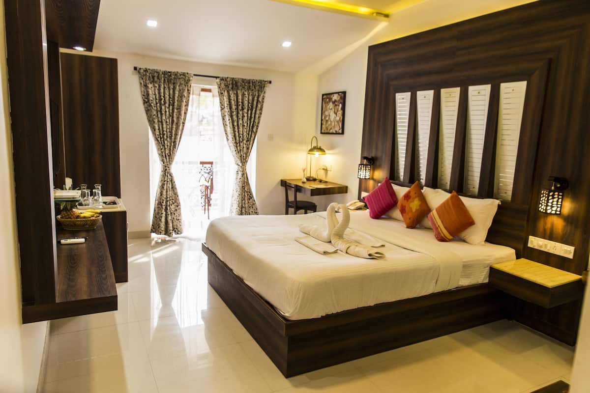 A hotel room with a large bed, a bedside table, a desk with a lamp, and a view of the outside through the curtains.