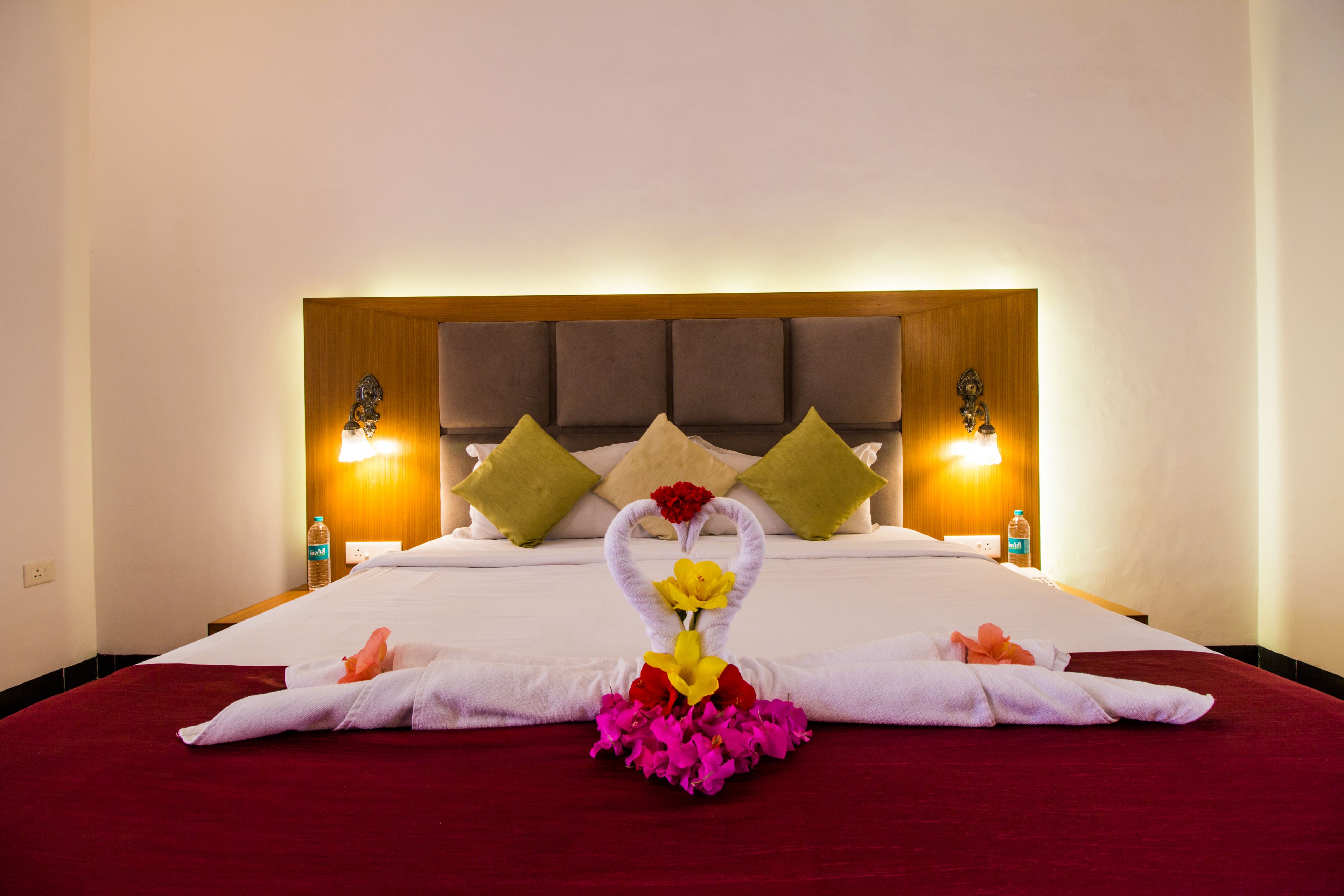 Una habitación de hotel con una cama grande, un cabecero de madera, dos lámparas de noche y un arreglo floral sobre la cama.