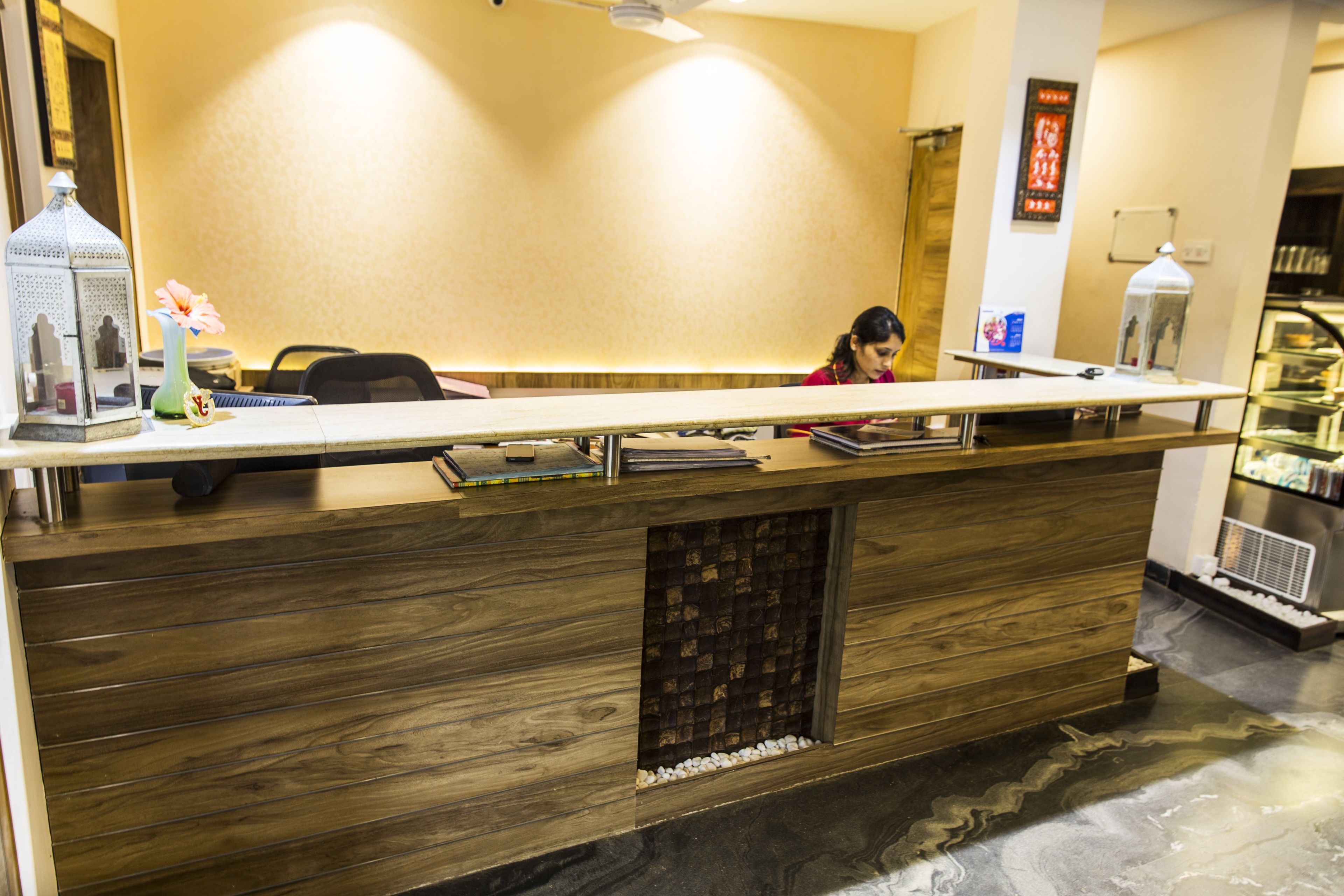 Un mostrador de recepción con detalles de madera, una pequeña fuente decorativa y una pantalla digital en la pared.