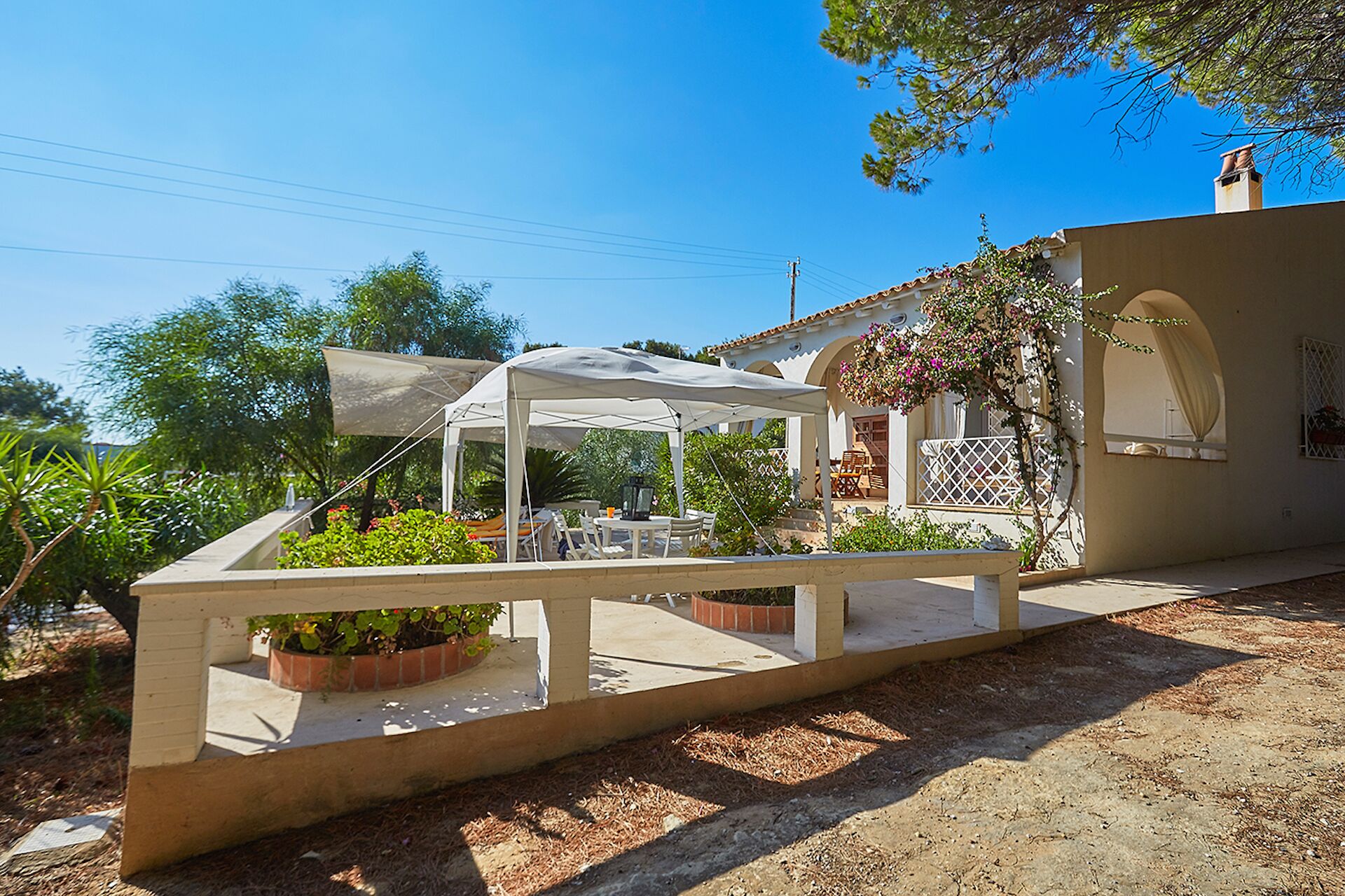 A patio area with a white umbrella, outdoor seating, and potted plants.