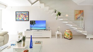 A modern living room with a flat-screen TV, white furniture, a staircase, and decorative plants. - Beachfront Las Burras MRA 02 by VillaGranCanaria (San Bartolomé de Tirajana)