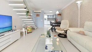 A modern living room with a flat-screen TV, a glass coffee table, a sofa, and a dining area in the background. - Beachfront Las Burras MRA 02 by VillaGranCanaria (San Bartolomé de Tirajana)