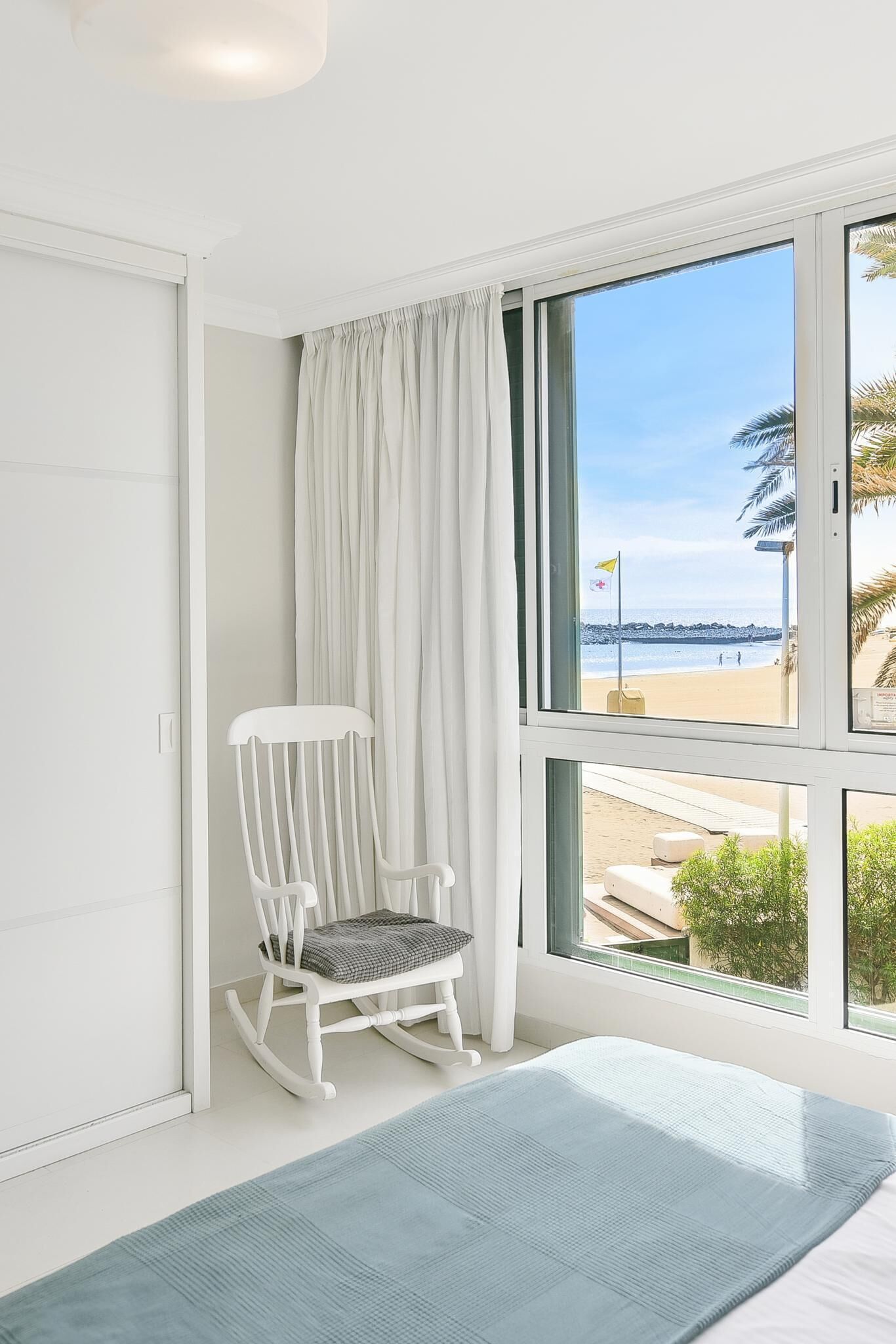 Una habitación con un ventanal grande, una mecedora y vista a la playa.